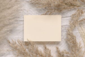 Blank card on white wooden table near dried pampas grass - ee220806