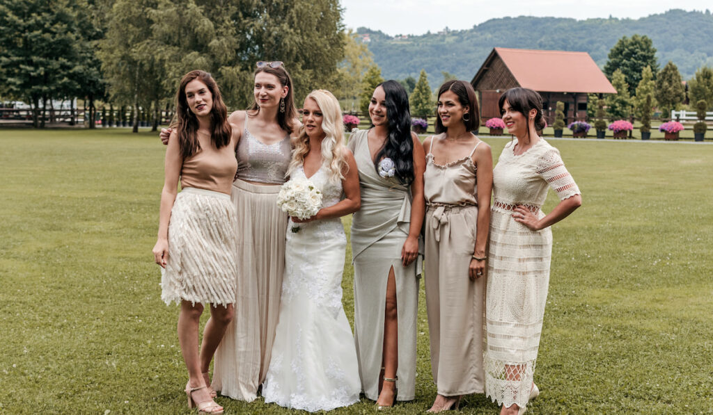 Bride and her bridesmaids standing and posing for a photo at a beautiful venue outdoors.
