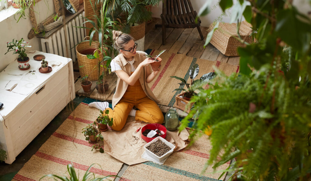 High angle view of young woman sitting on the floor and busy with transplantation of flowers and plants in the flower garden


