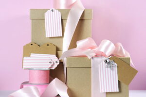 Modern trend natural gift wrapping with natural brown kraft paper boxes and pale pink ribbon with pink and white gift tags against a pink and white background - ss220806