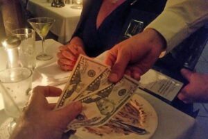 Senior man hands money to waiter at end of meal in restaurant as wife watches - ee220806