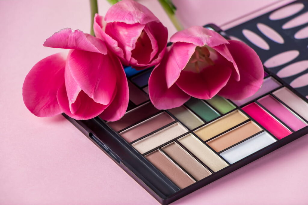 Set of cosmetics and flowers on a pink background.