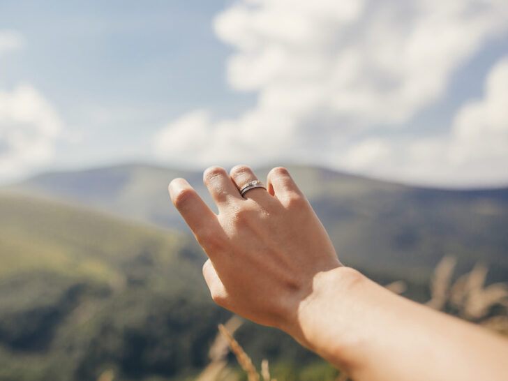 Traveler hand reaching out to mountains with engagement ring