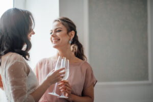 Two millennial candid lifestyle brunette girls in bridal outfits are having fun drinking champagne - ee220806