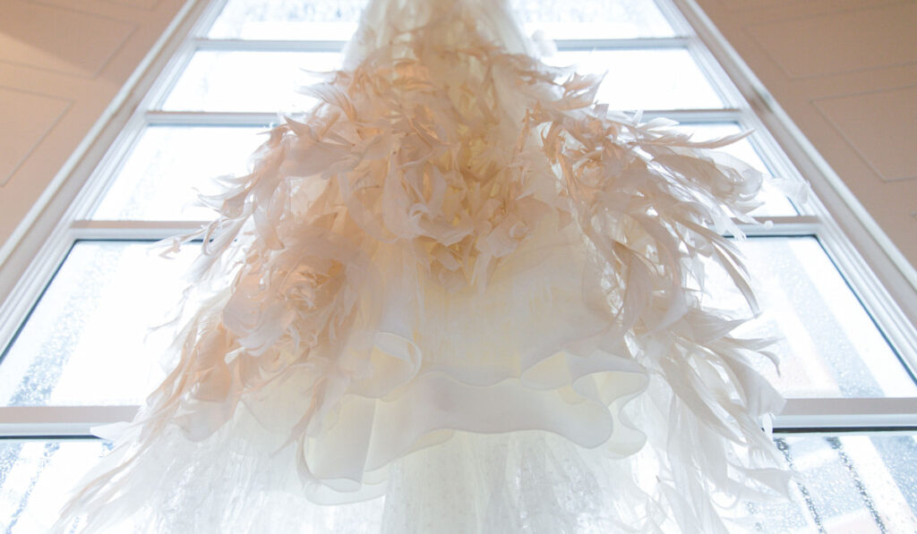 Wedding dress with feathers hanging near the window