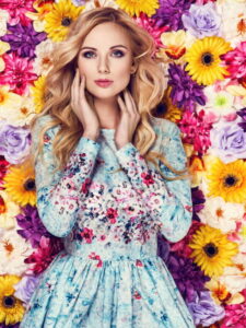 Beautiful young woman in nice blue dress posing on colorful wall of flowers - ss220803