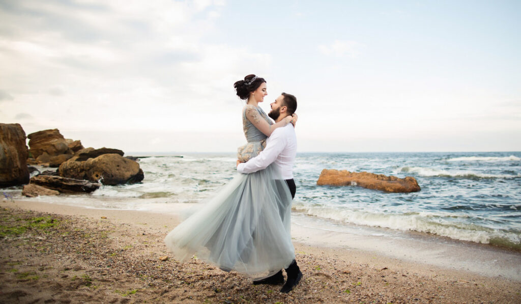 newly wed having fun by the sea, beach wedding concept, bride wearing light blue wedding dress