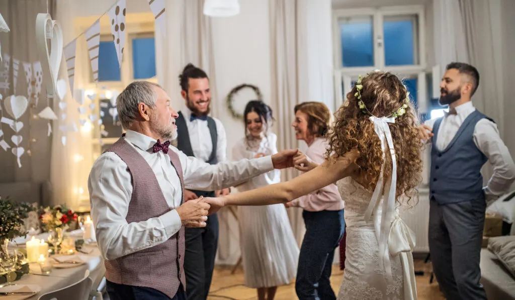 A young bride dancing with grandfather and other guests on a wedding reception.
