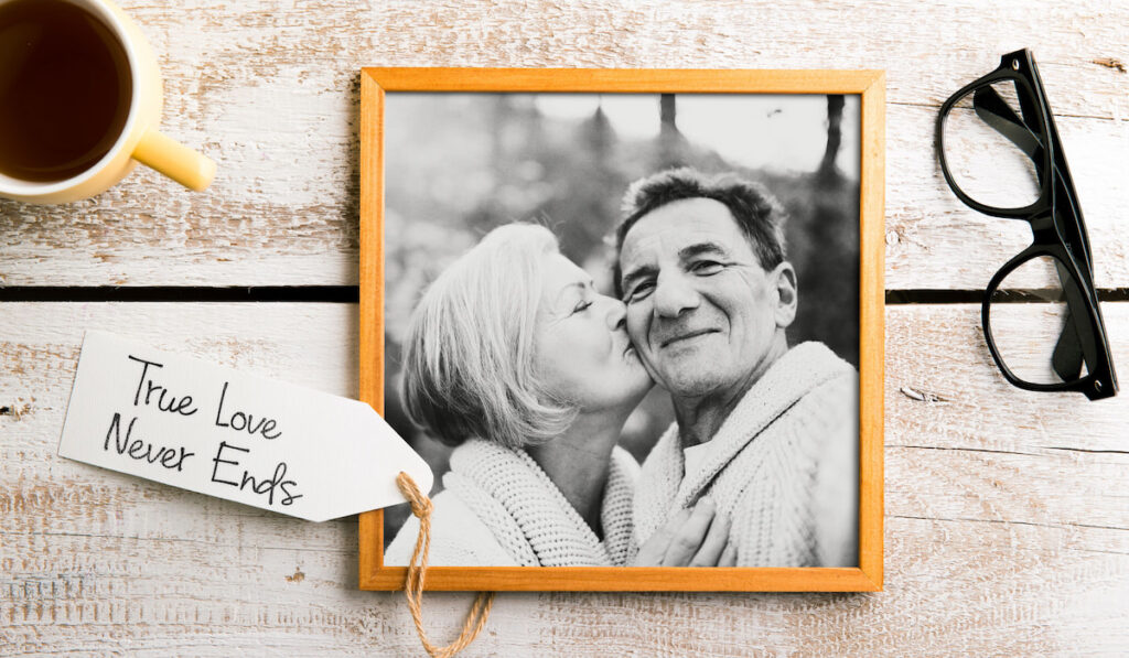 Black and white photo of elderly couple in picture frame with tag true love never ends on wooden table