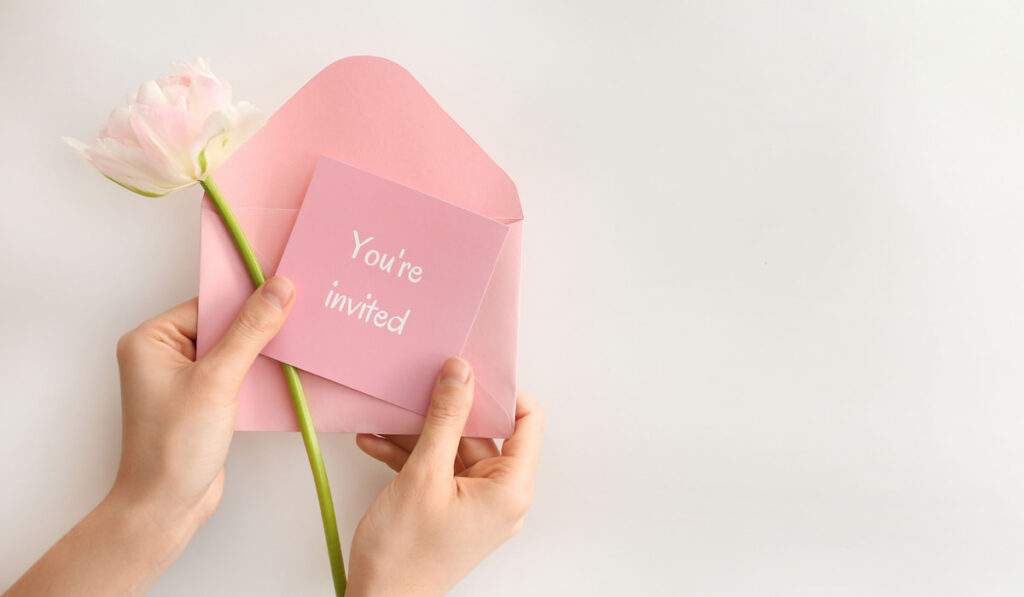 Female hands with pink invitation an pink flower on white background