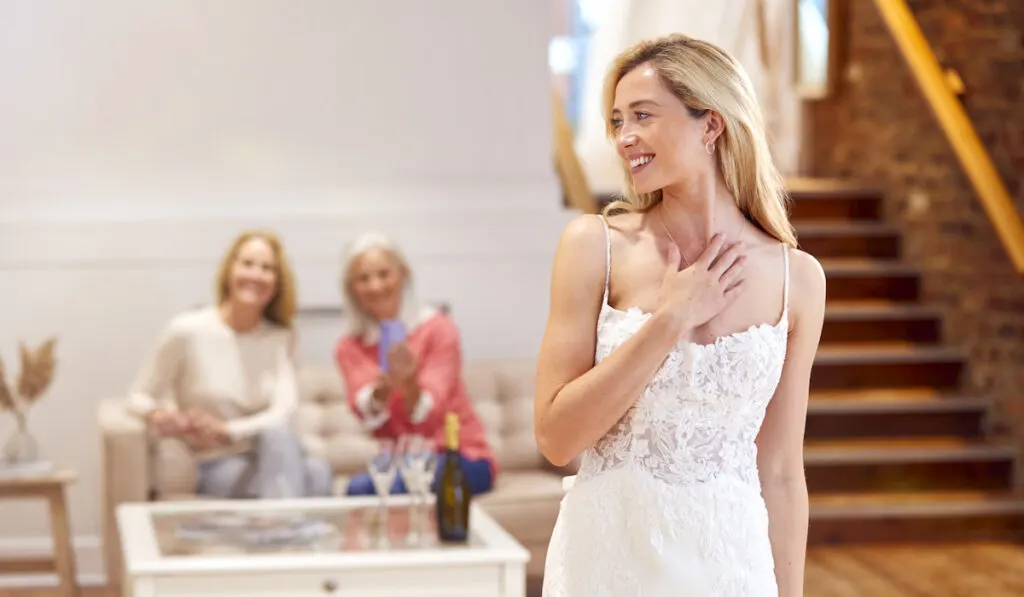Grandmother with mother watching daughter bride trying on the wedding dress