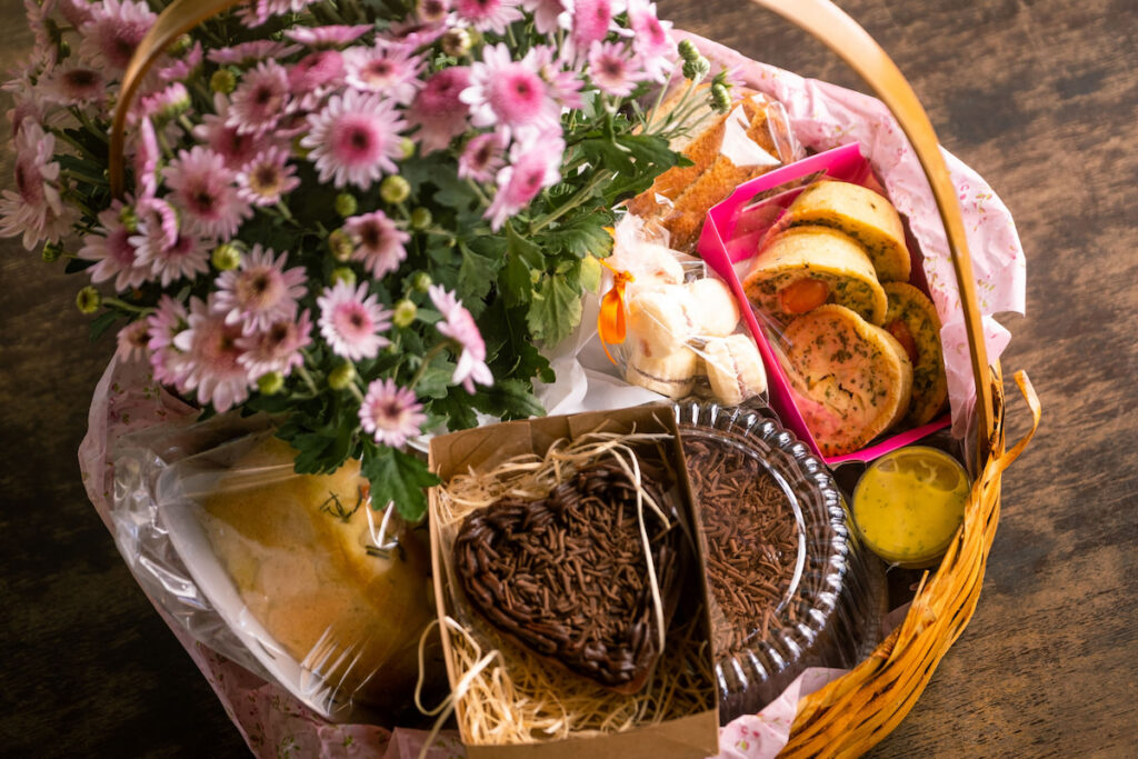 Heritage basket with chocolate, quiches, cheese, and flowers on a wooden table 