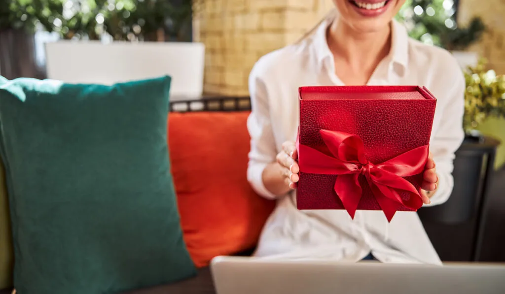 Smiling woman sitting on the sofa with gift in hands
