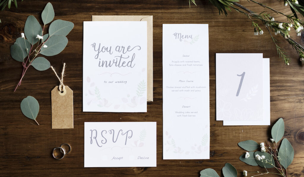 Wedding Invitation Cards Papers Laying on Table Decorate With Leaves
