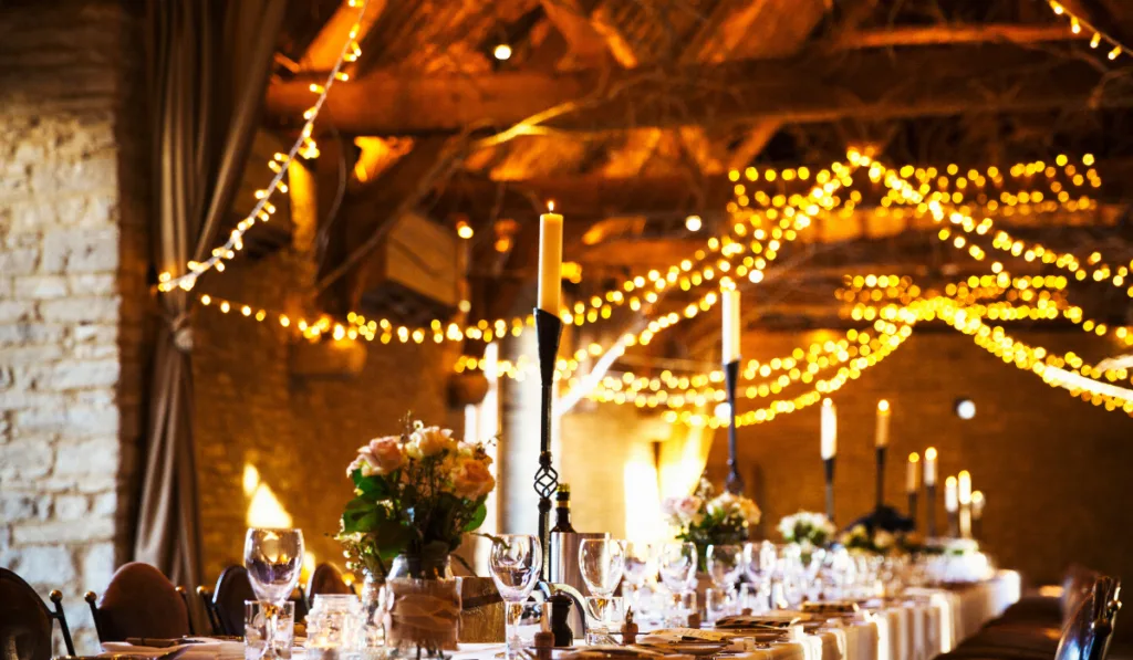A wedding venue decorated for a party, with fairy lights and the tables set for dinner.
