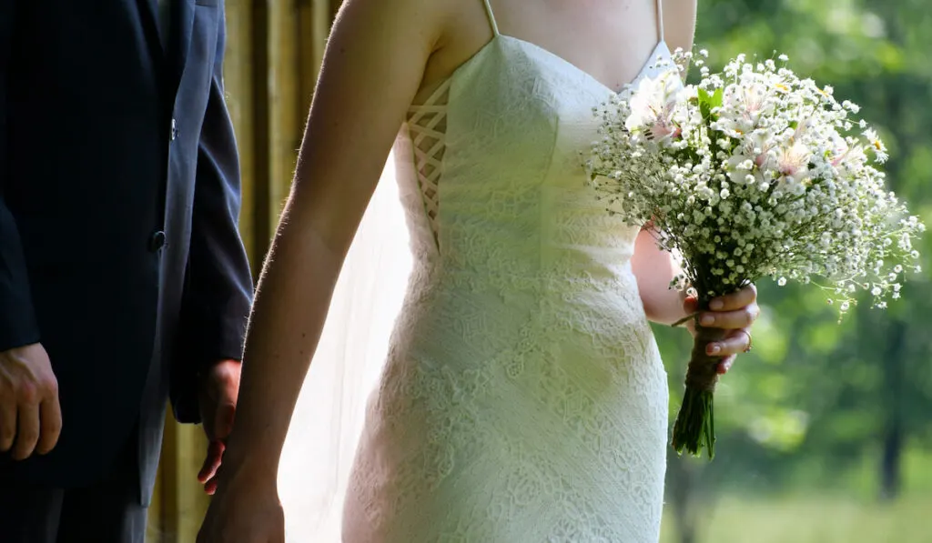 A bride with a bouquet of daisies and baby's breath flowers walking with her groom on the side