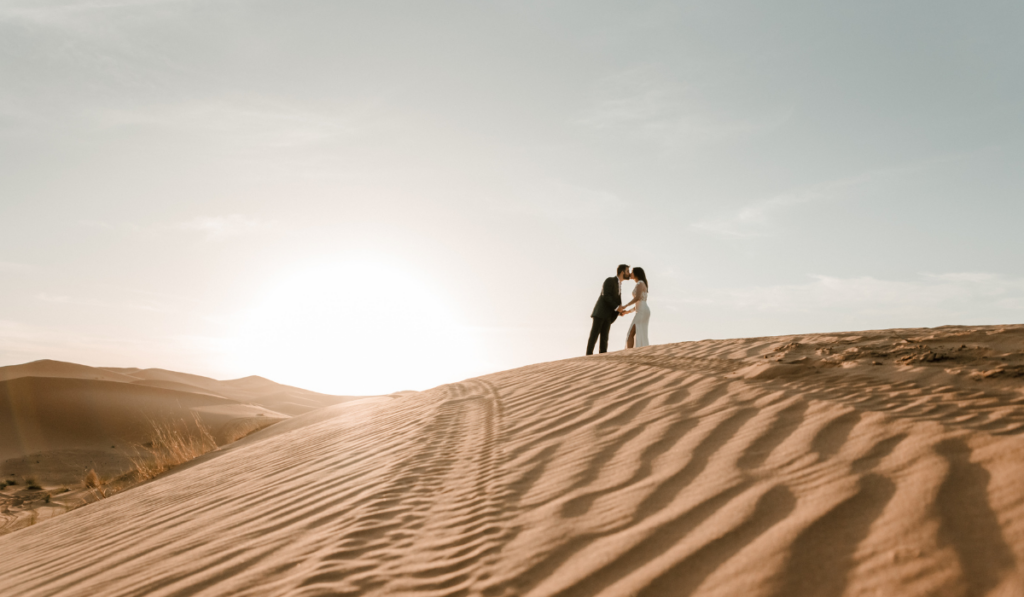 A newly wed couple kissing on top of a desert sand dune at dawn
