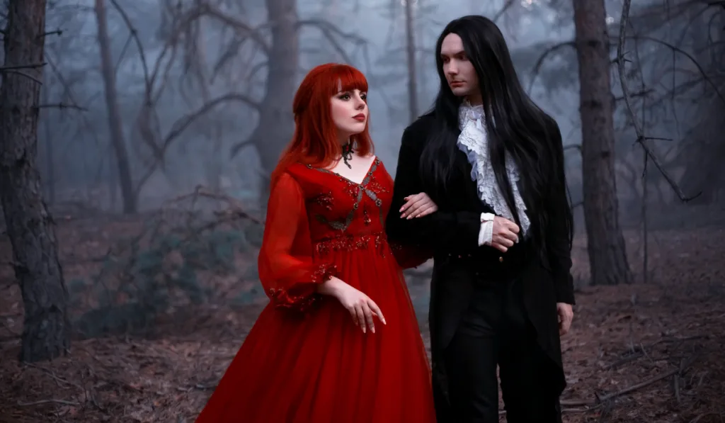dark wedding theme in the forest, bride wearing a red wedding dress matching her red hair, groom wearing a black coat and pants with a long hair