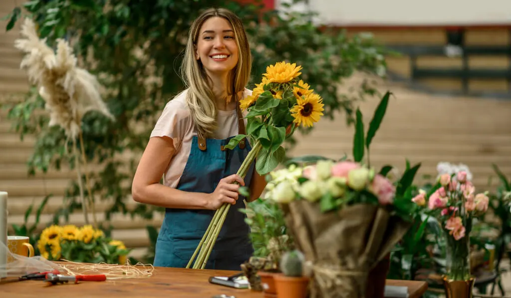 Happy Woman florist standing and holding bouquet of sunflowers in flower shop
