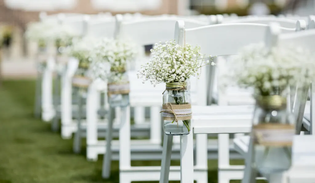 Jar with white flowers hanging from chairs on a wedding venue