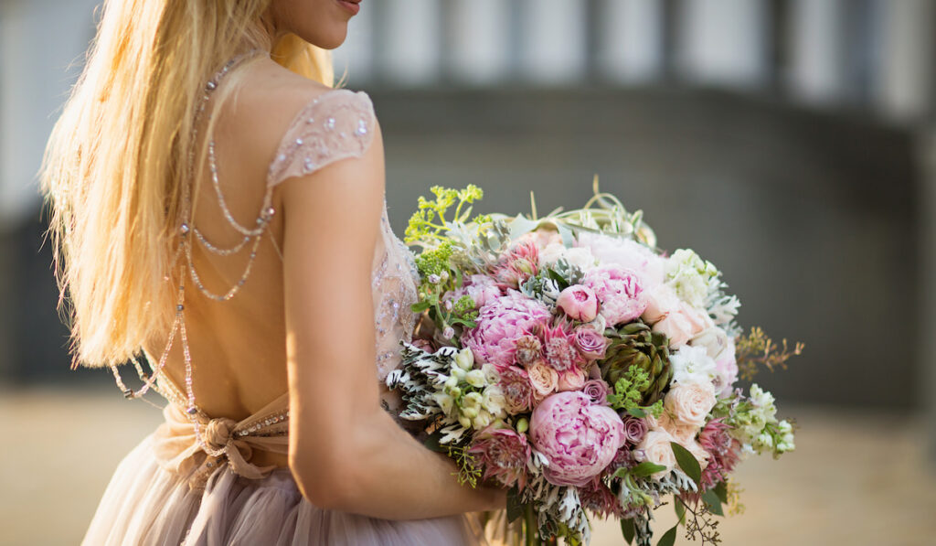 Portrait of elegant bride wearing wedding dress and holding bouquet of pastel flowers