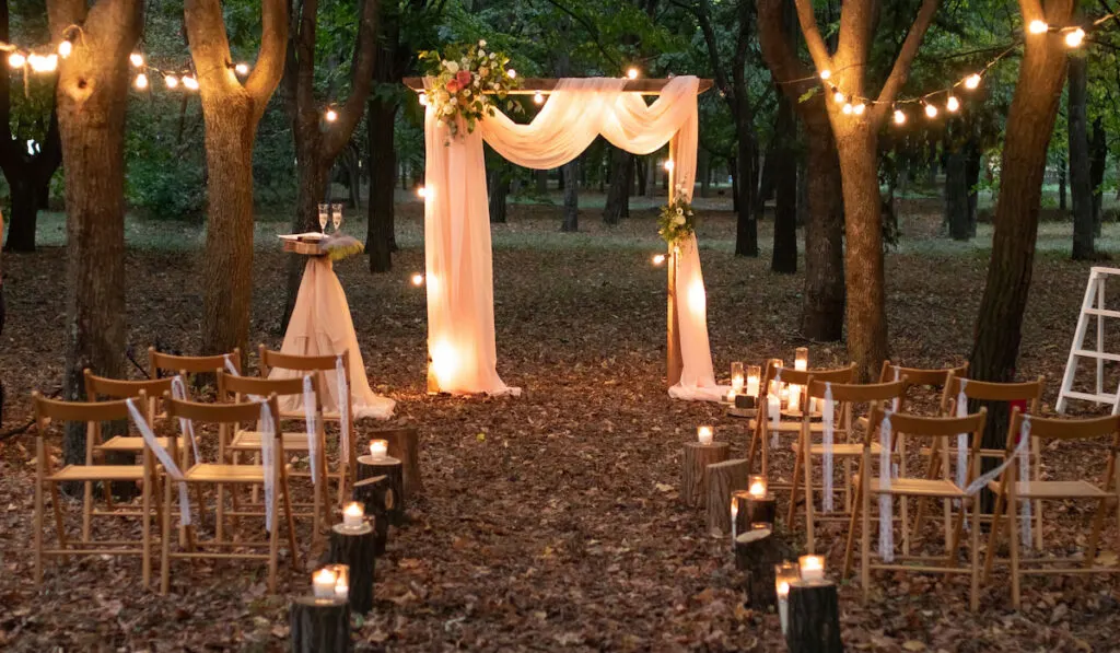 Wedding arch in the woods with light bulbs and candle decoration, rustic wedding in the forest