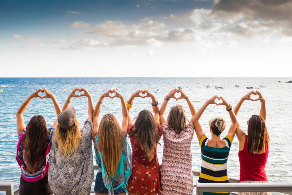 girls from the backside doing a heart with the hands looking at the ocean waiting the sunset in vacation leisure activity