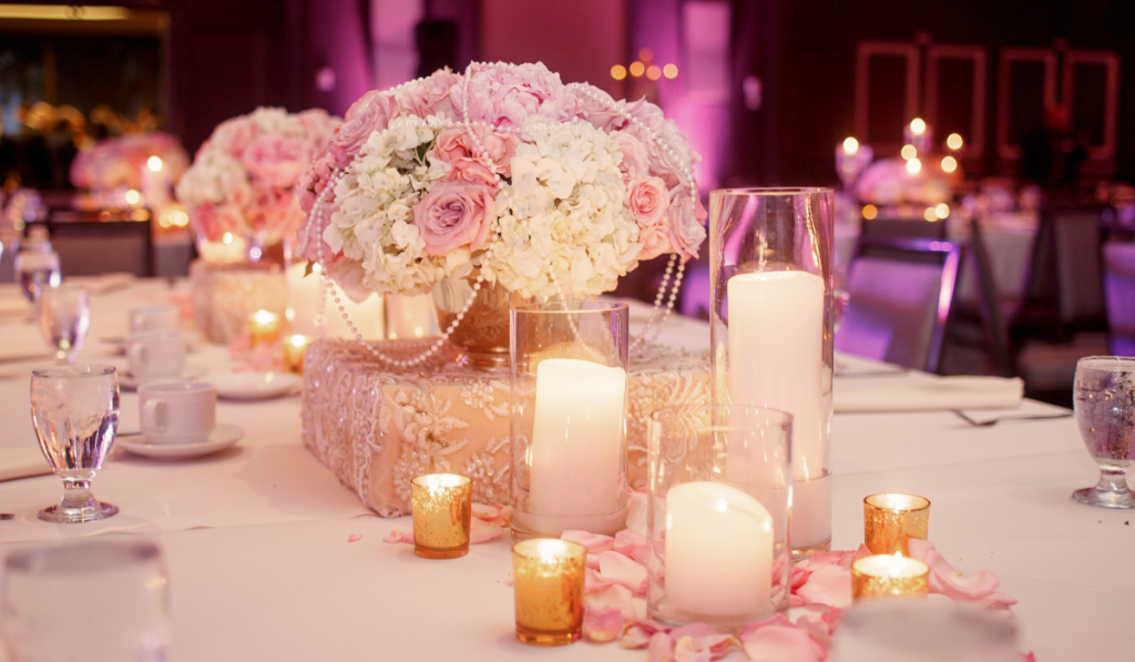 Lighted white candles stand around luxury pink rose bouquet on a table
