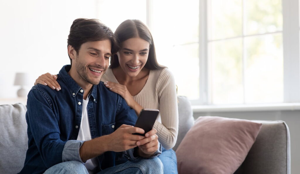 Smiling young couple at smartphone together, have video call 