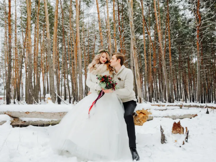 bride and groom posing for their winter wedding photo session outdoors in a forest with white snow on the ground