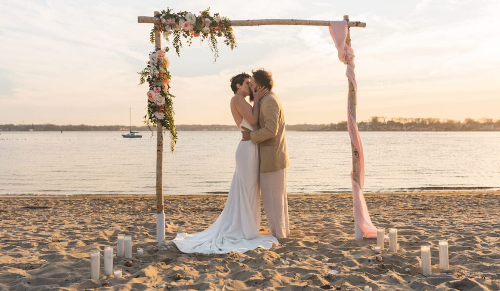 A bride and groom have an intimate beach wedding in summer with a decorative arch
