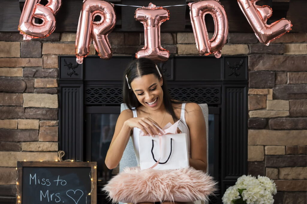American woman opening a bridal shower present with pink bride balloons 