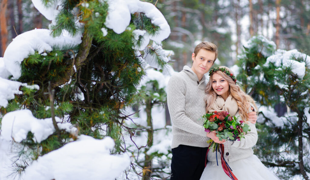 Bride and groom standing near tree in the winter forest, winter wedding ceremony