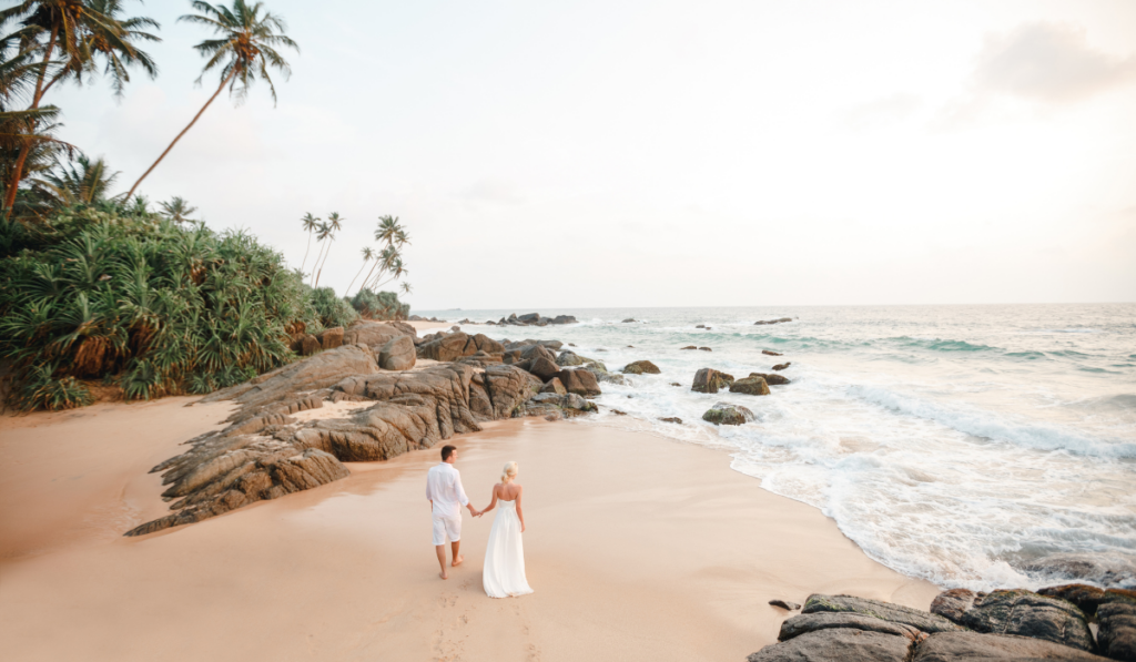 Back view of wedding couple is running on the sea beach. Sunny summer photo. Bride with groom on tropical beach