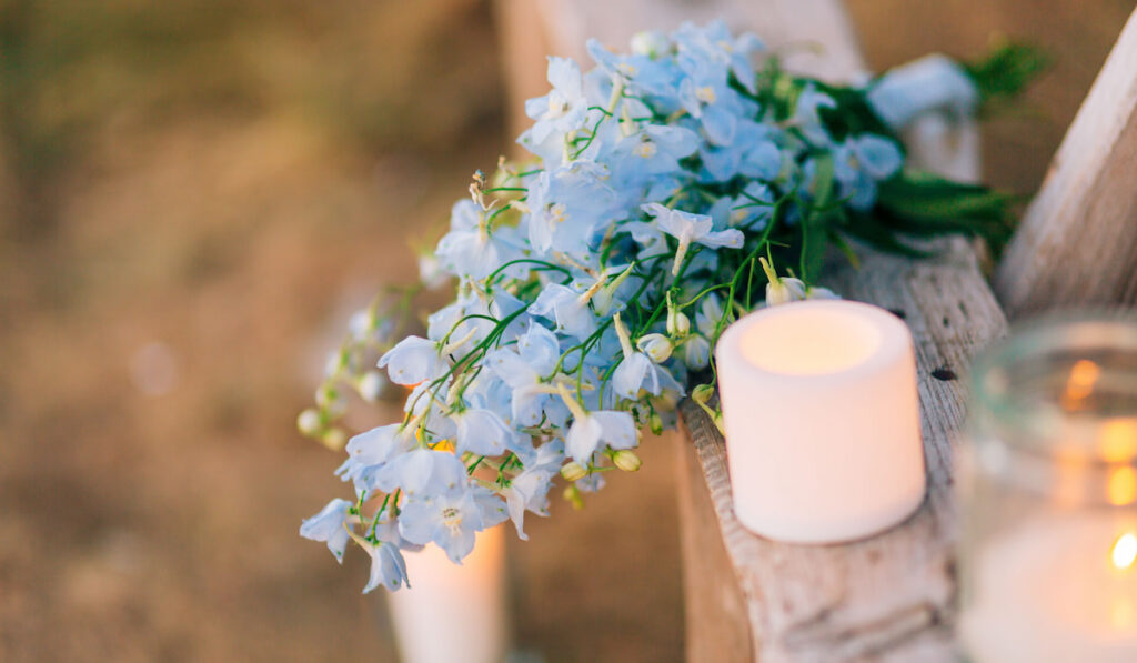 wedding bridal bouquet of blue delphinium on an old wooden bench with candles on the side